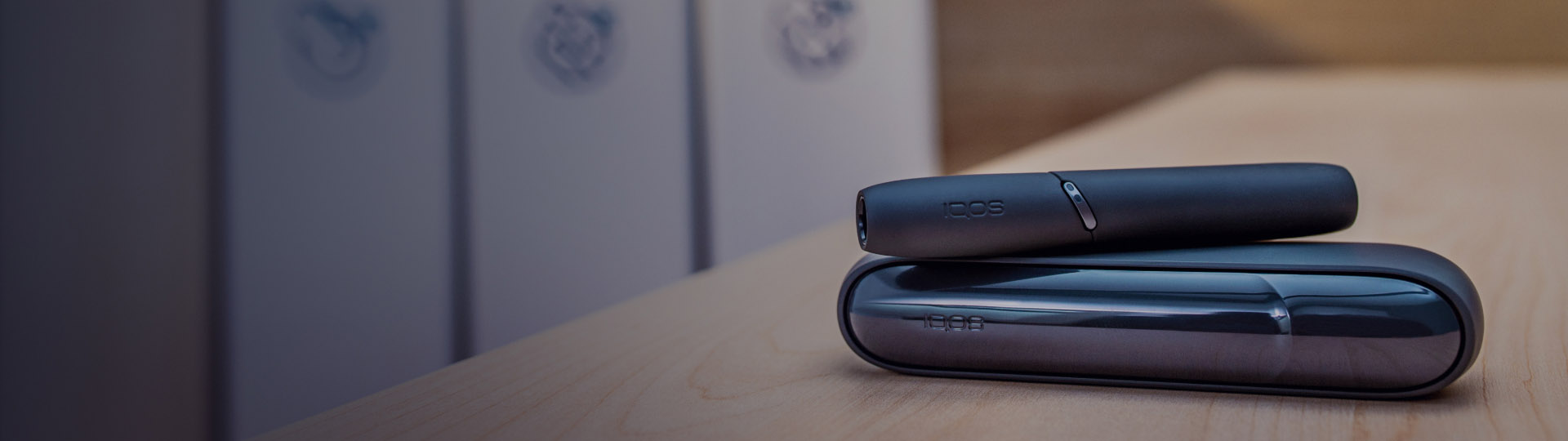Dark blue IQOS device on a table. Recycling containers in the background.