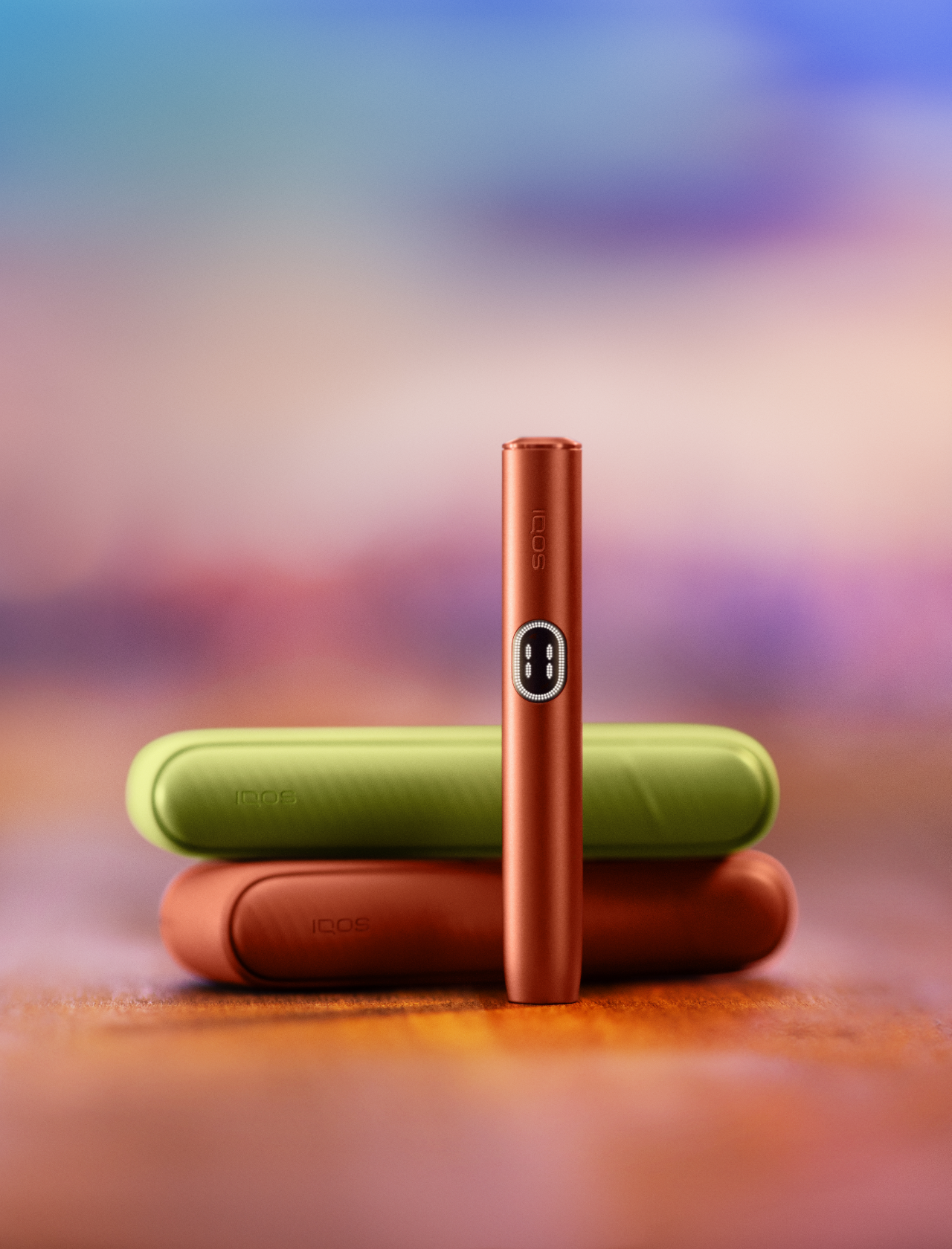 Red IQOS ILUMA i device standing in front of three different coulours chargers