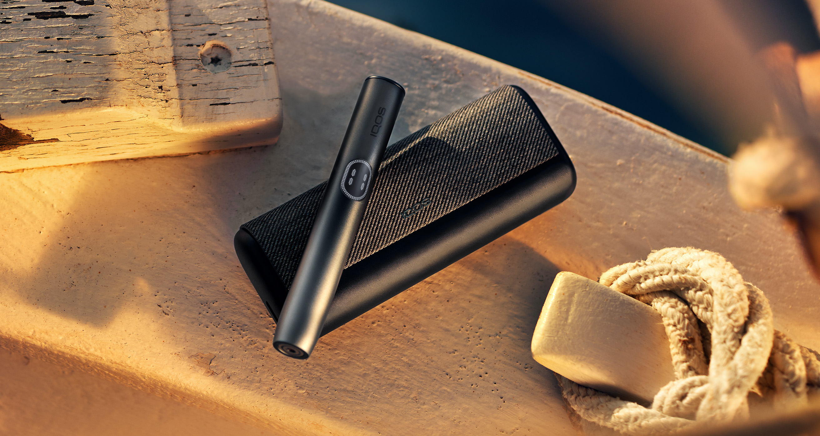 Midnight Black IQOS ILUMA i PRIME device with holder on top of it, on a wooden background